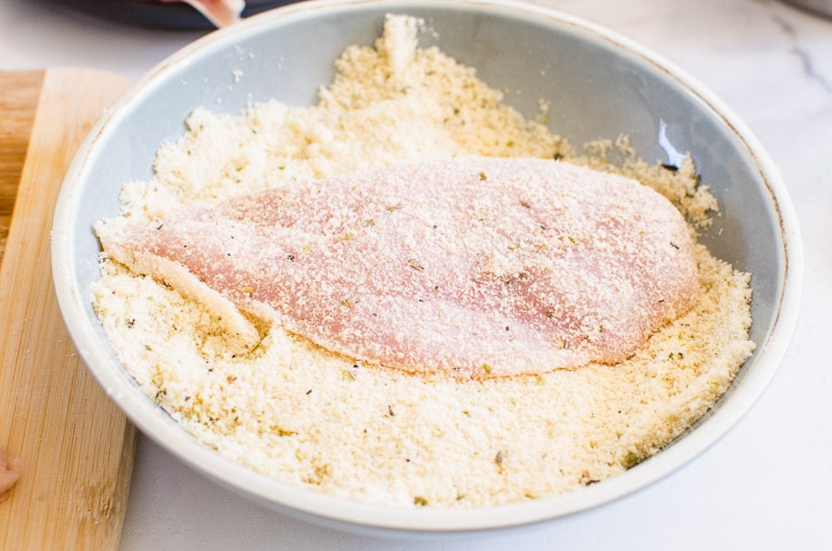 Raw chicken breast in bowl with breading.