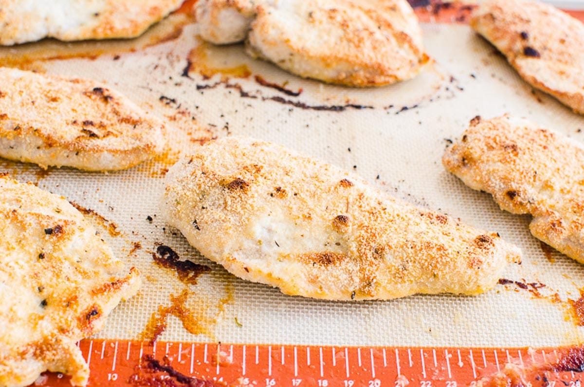 Baked chicken breast cutlets on silpat lined baking sheet.