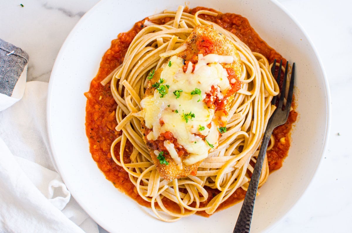 Healthy baked chicken parmesan in a deep bowl with noodles and tomato sauce.