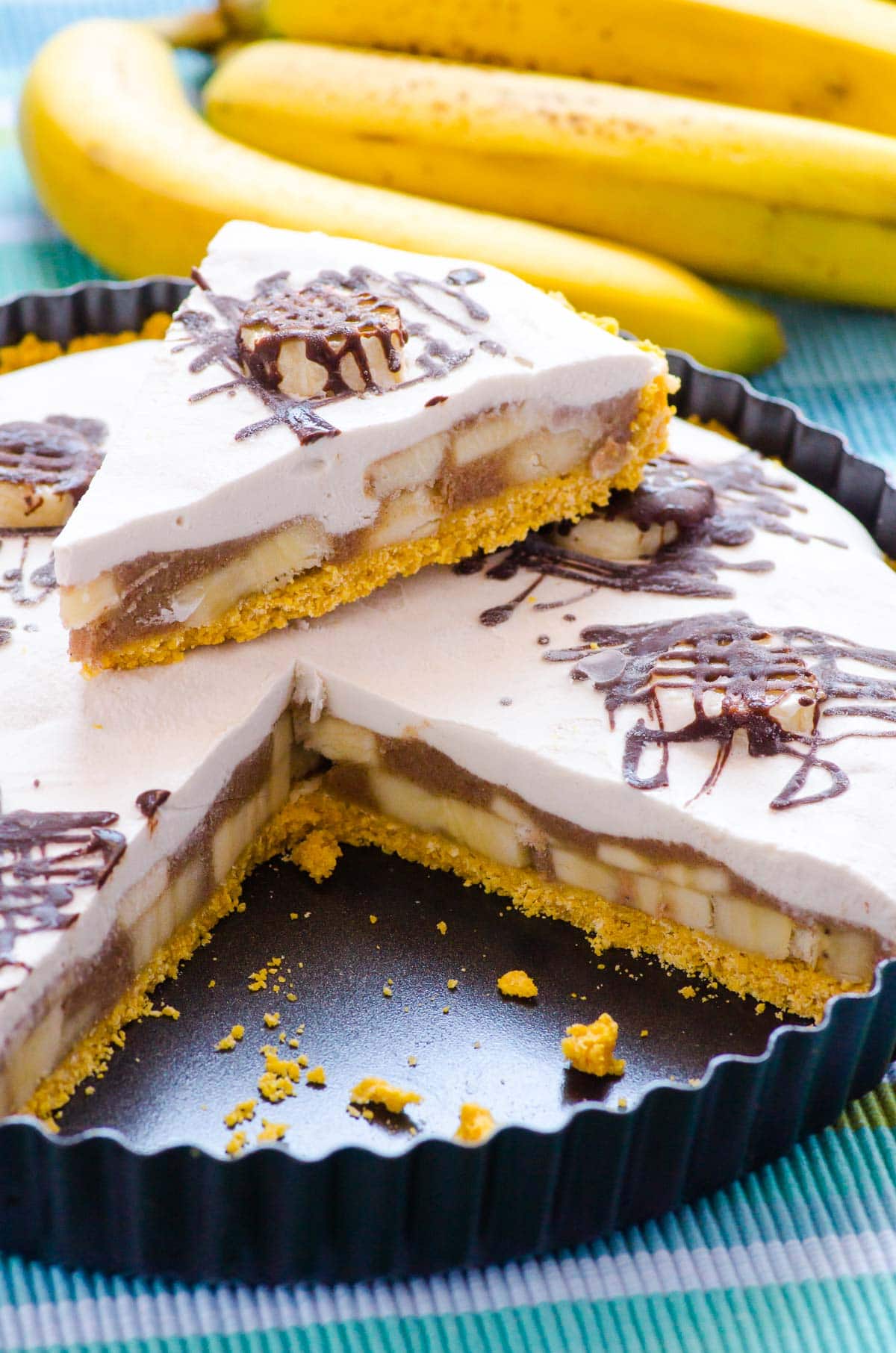 Healthy banana cream pie slice on top of a pie in a dish and bananas nearby.