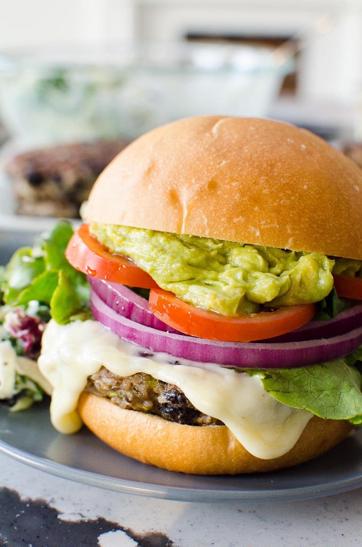 Healthy black bean burgers on bun with cheese, onion, tomato and guacamole.