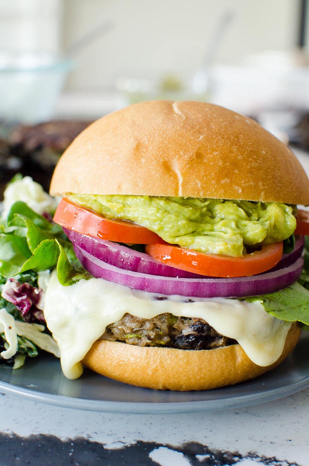 Healthy black bean burgers on bun with cheese, onion, tomato and guacamole.