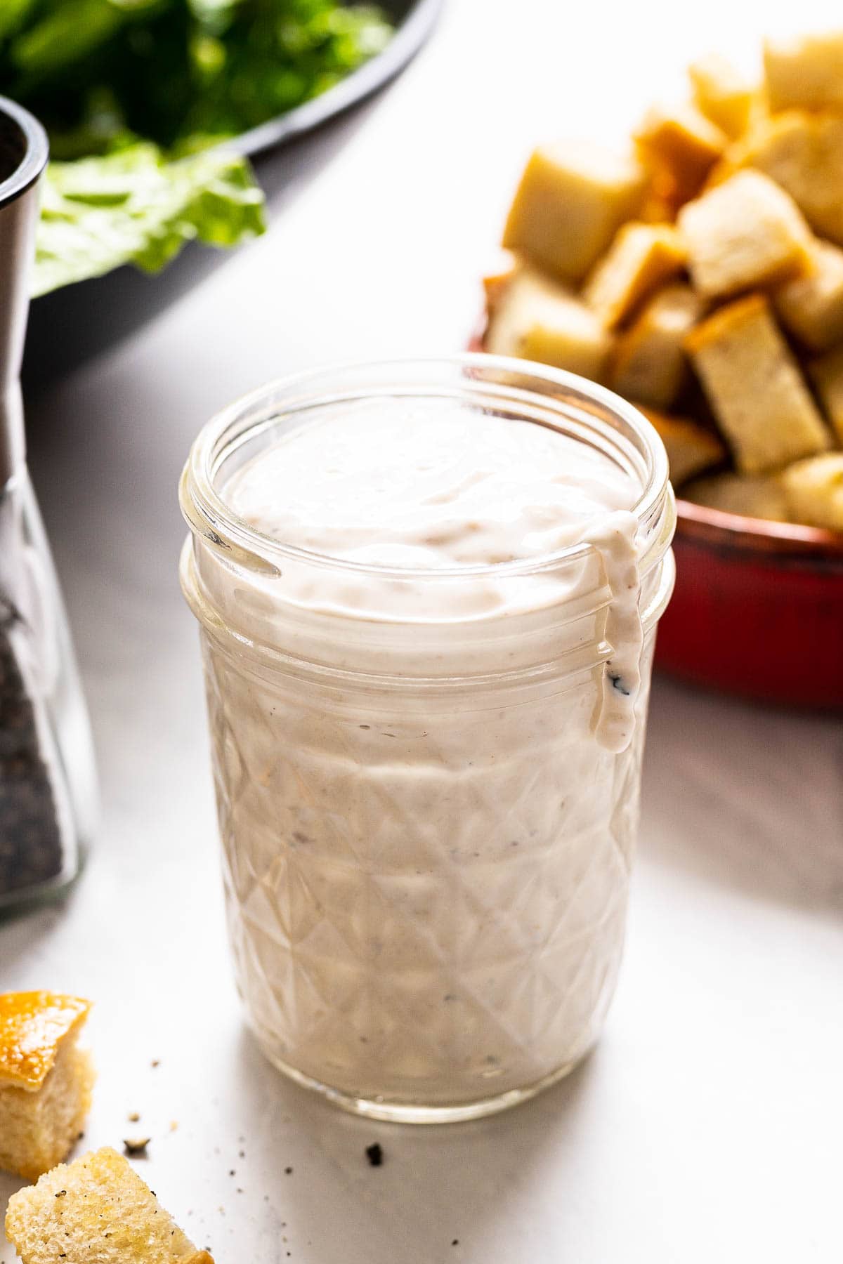 Healthy caesar dressing with Greek yogurt in a glass jar, croutons and salad behind