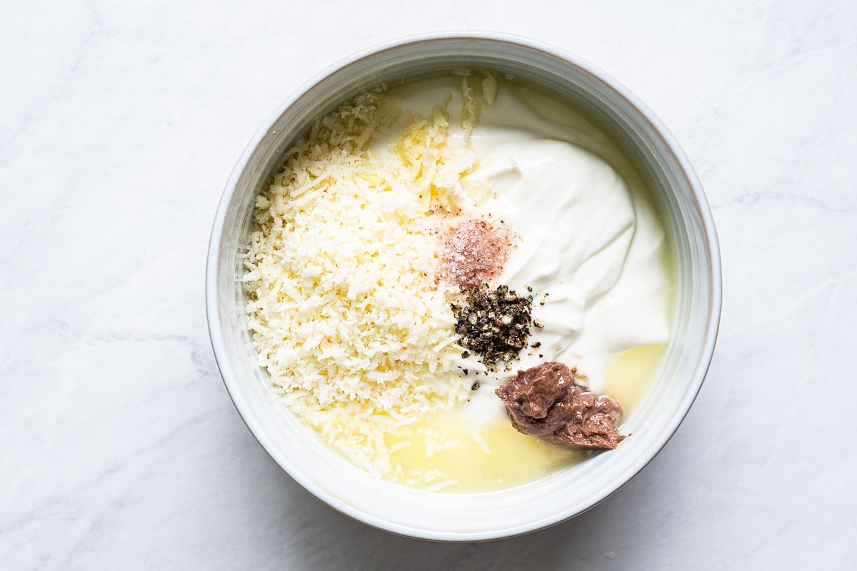 Yogurt, parmesan, anchovy paste, salt, pepper, garlic and lemon juice in a bowl.