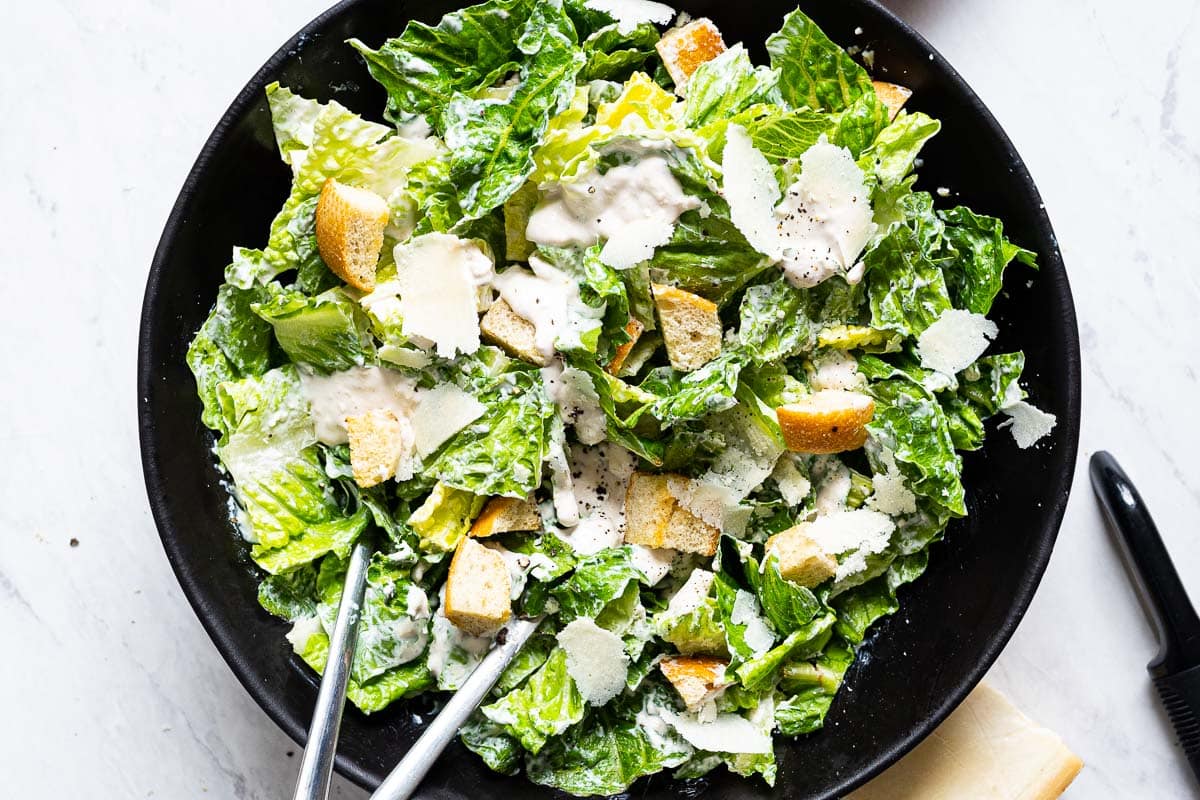 Healthy caesar salad tossed with dressing, croutons and dressing in bowl.