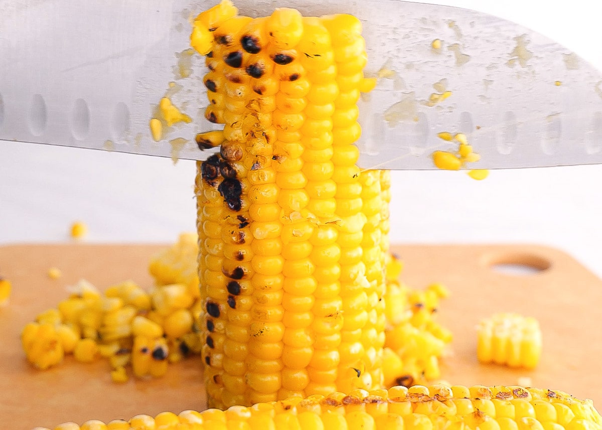 Removing corn kernels from a corn husk with a knife.