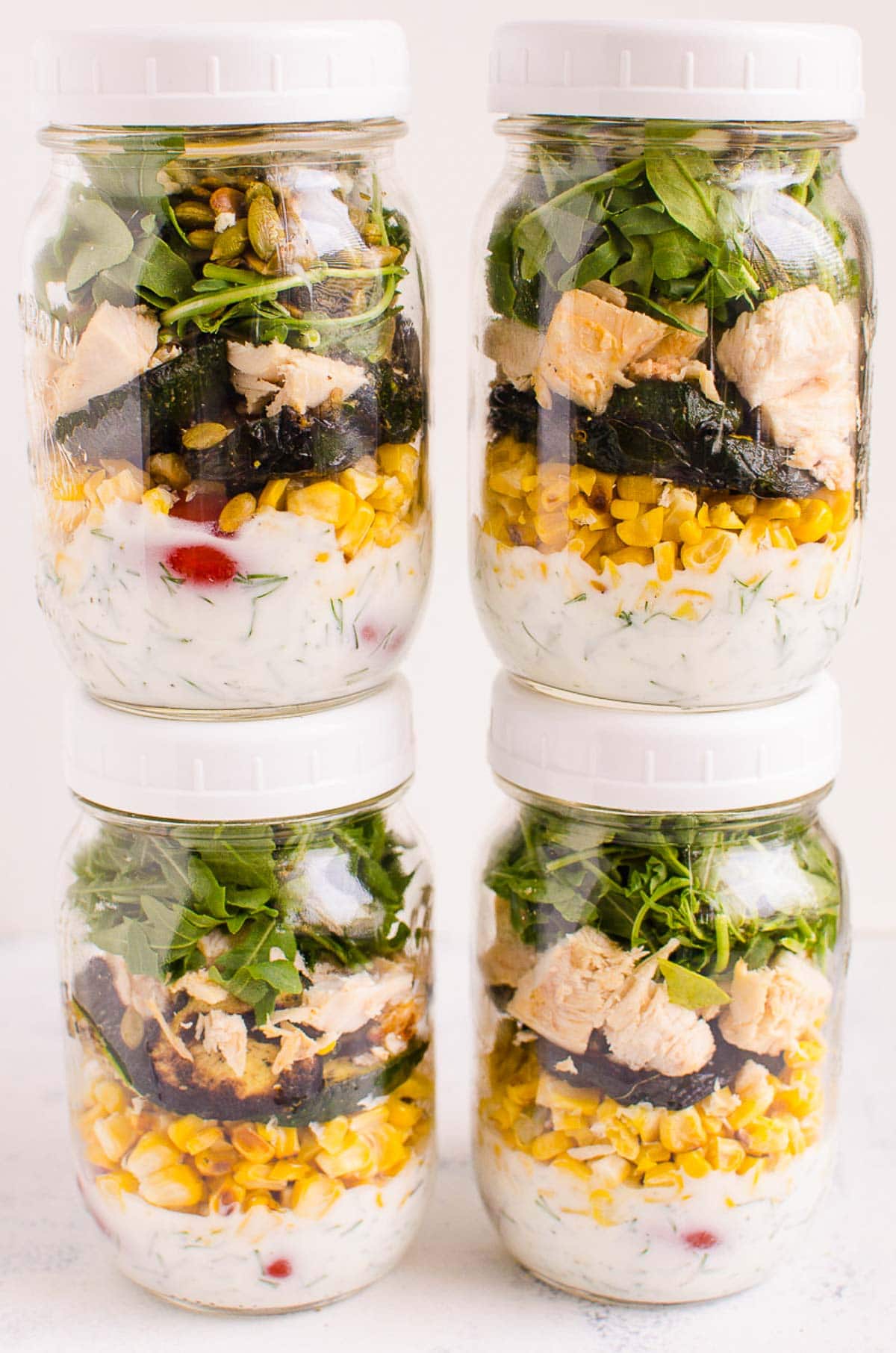 Healthy cobb salad assembled in four mason jars with lids and stacked on top of each other.