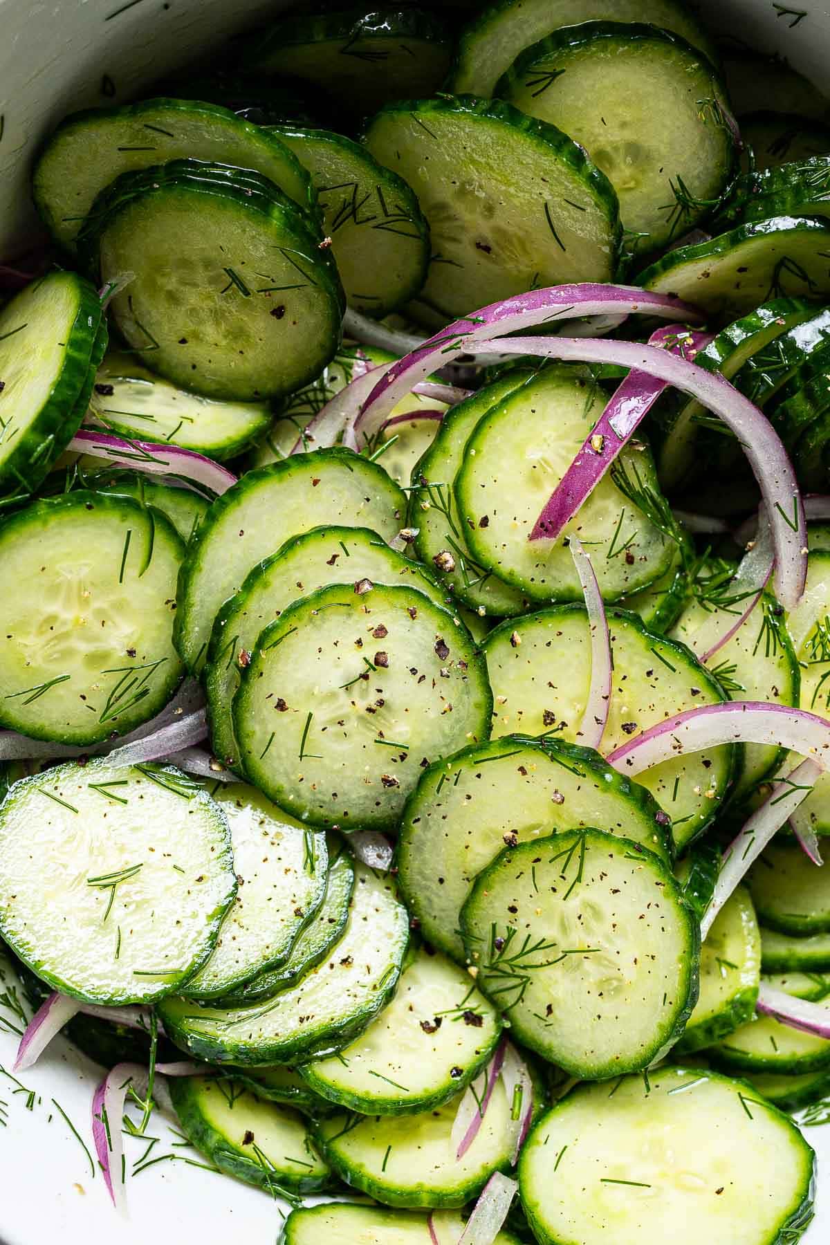 Closeup of healthy cucumber salad with red onions, dill, salt and pepper.