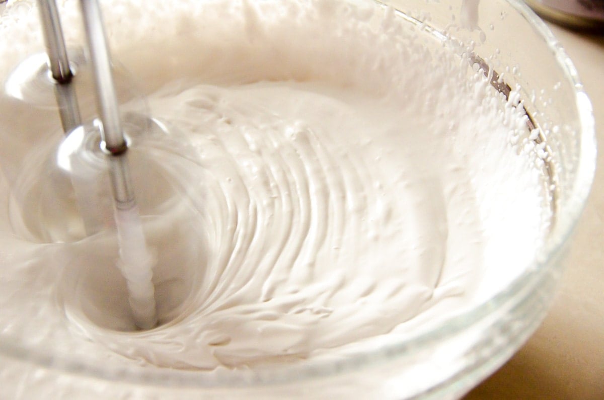 Whipping coconut cream with a hand mixer in glass bowl.