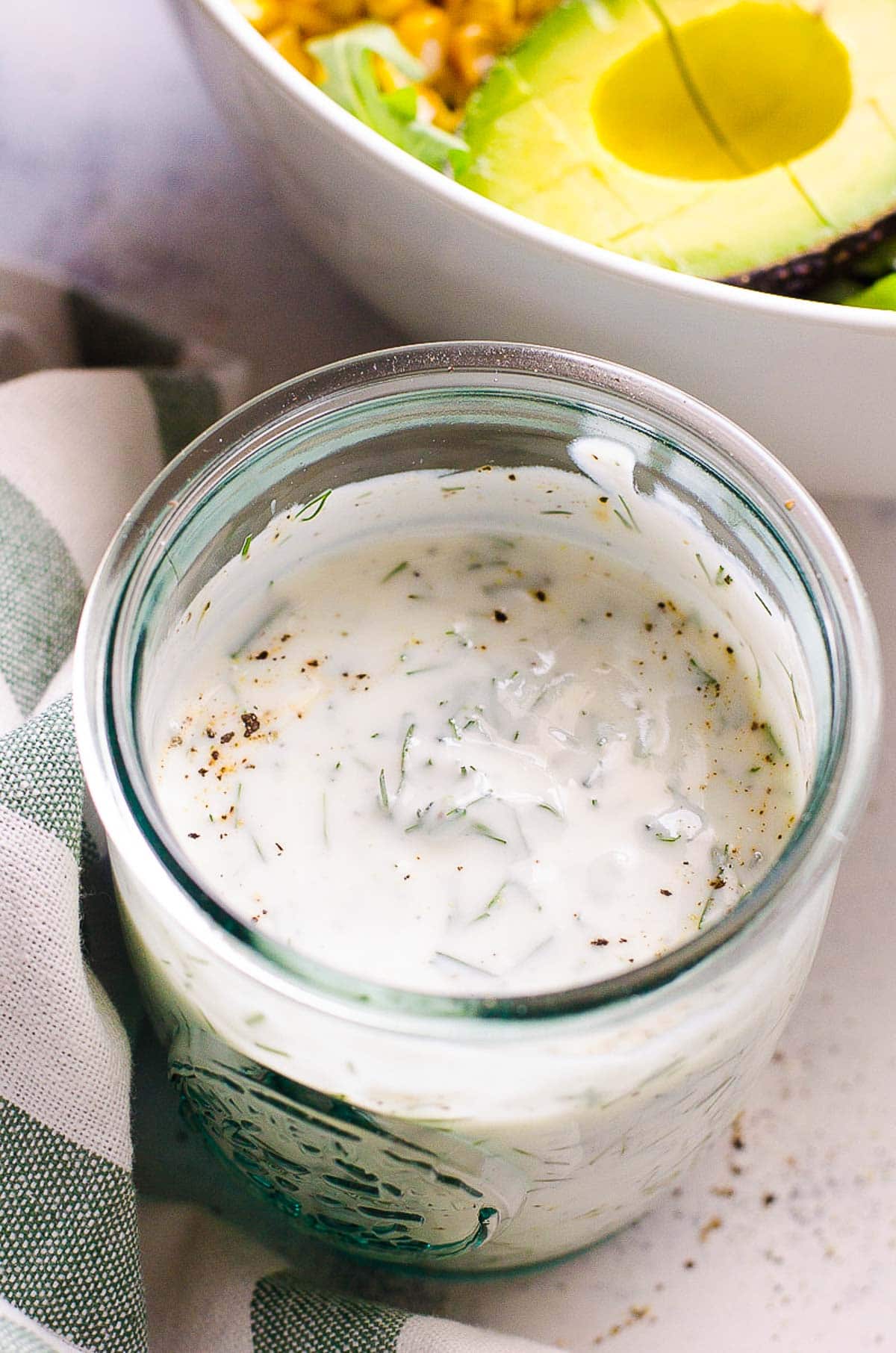 Healthy ranch dressing with Greek yogurt in a glass jar next to a salad bowl.