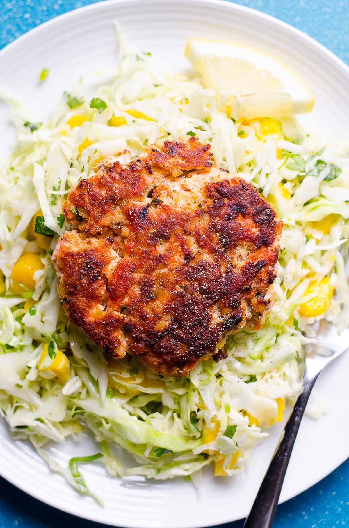 One healthy salmon burger on a plate served over mango coleslaw.