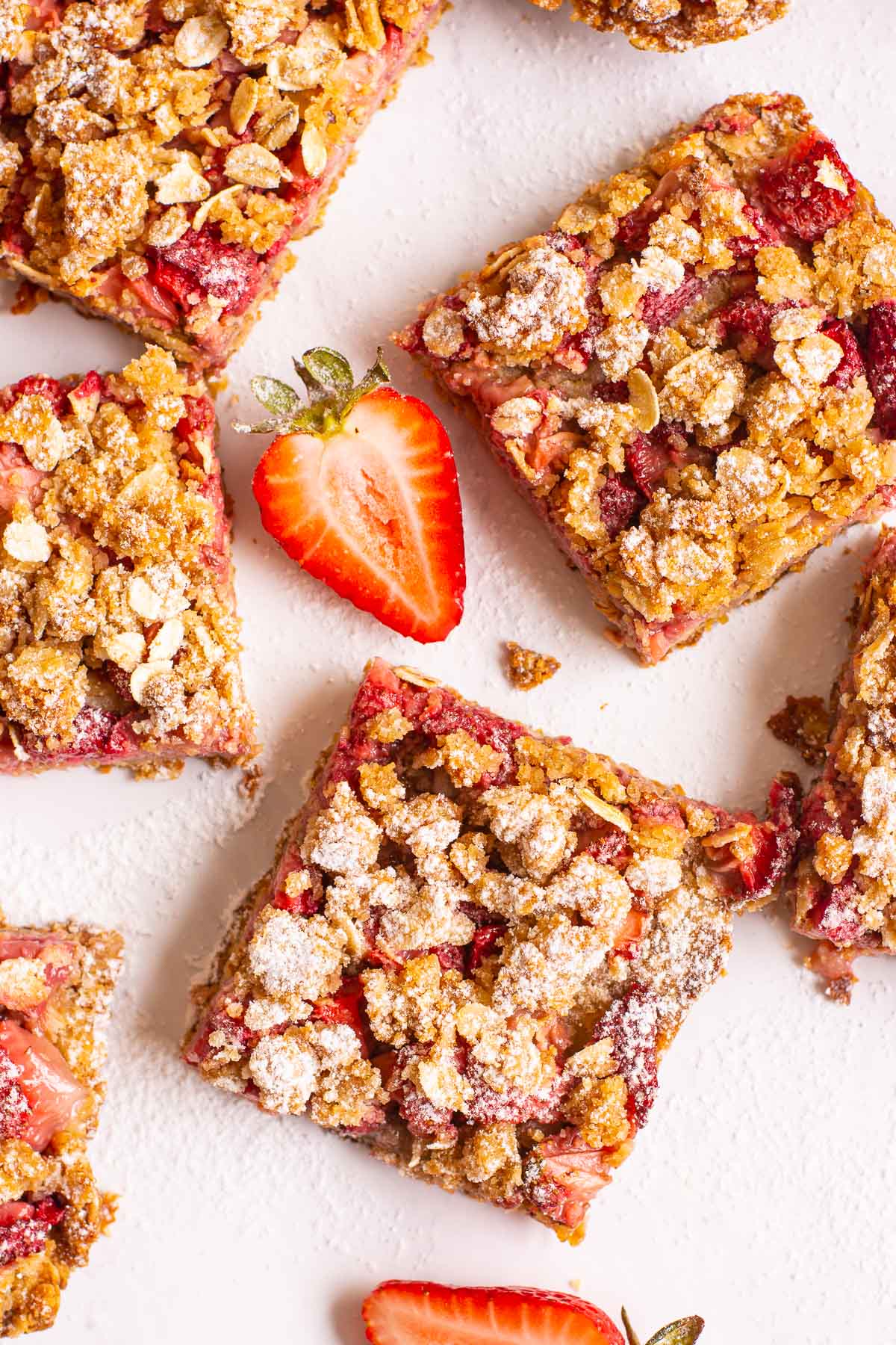 Healthy strawberry oatmeal bars with icing sugar and sliced strawberry on the counter.