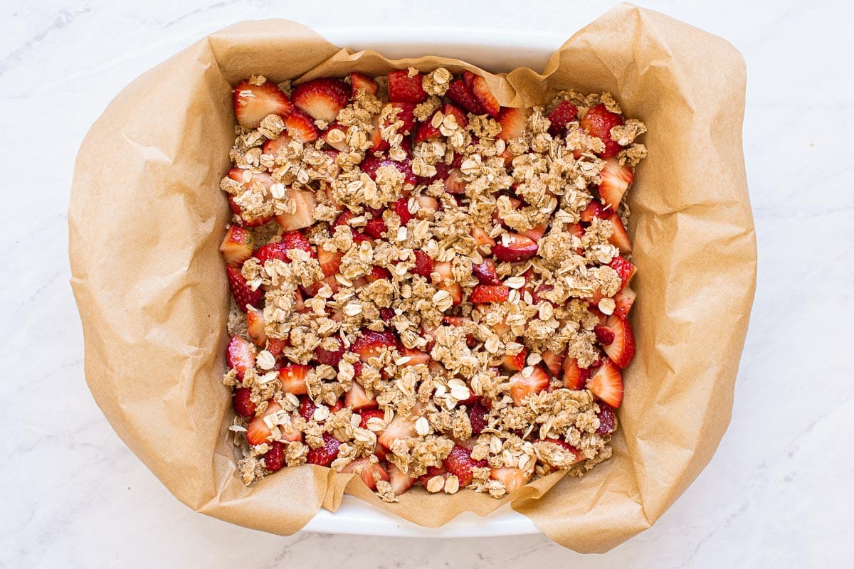 Parchment lined baking pan filled with strawberries and oat crumble topping.