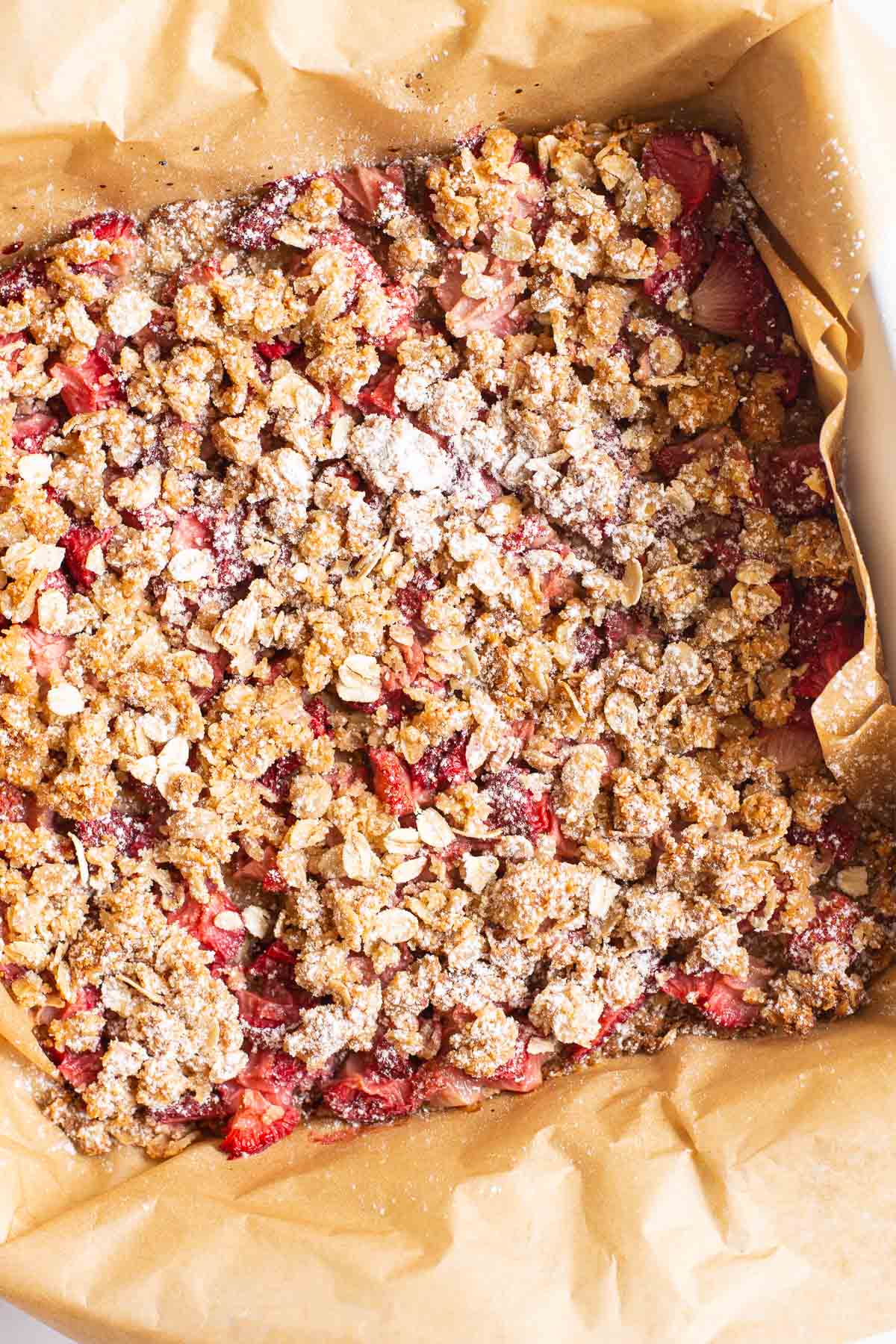 Healthy strawberry oatmeal bars in a pan lined with parchment paper and sprinkled with icing sugar.