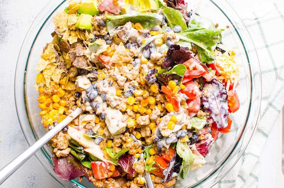 Healthy taco salad being mixed together in a large bowl.