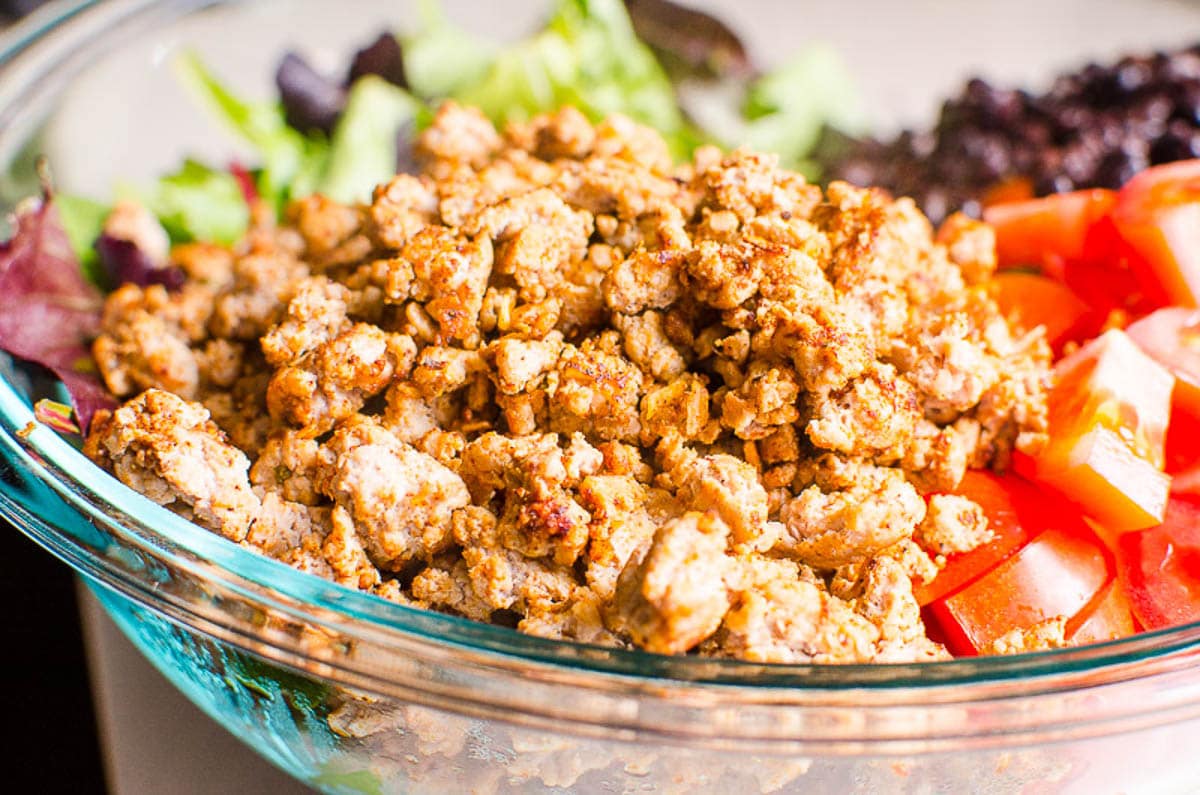 Ground turkey meat in a bowl with tomatoes and lettuce.