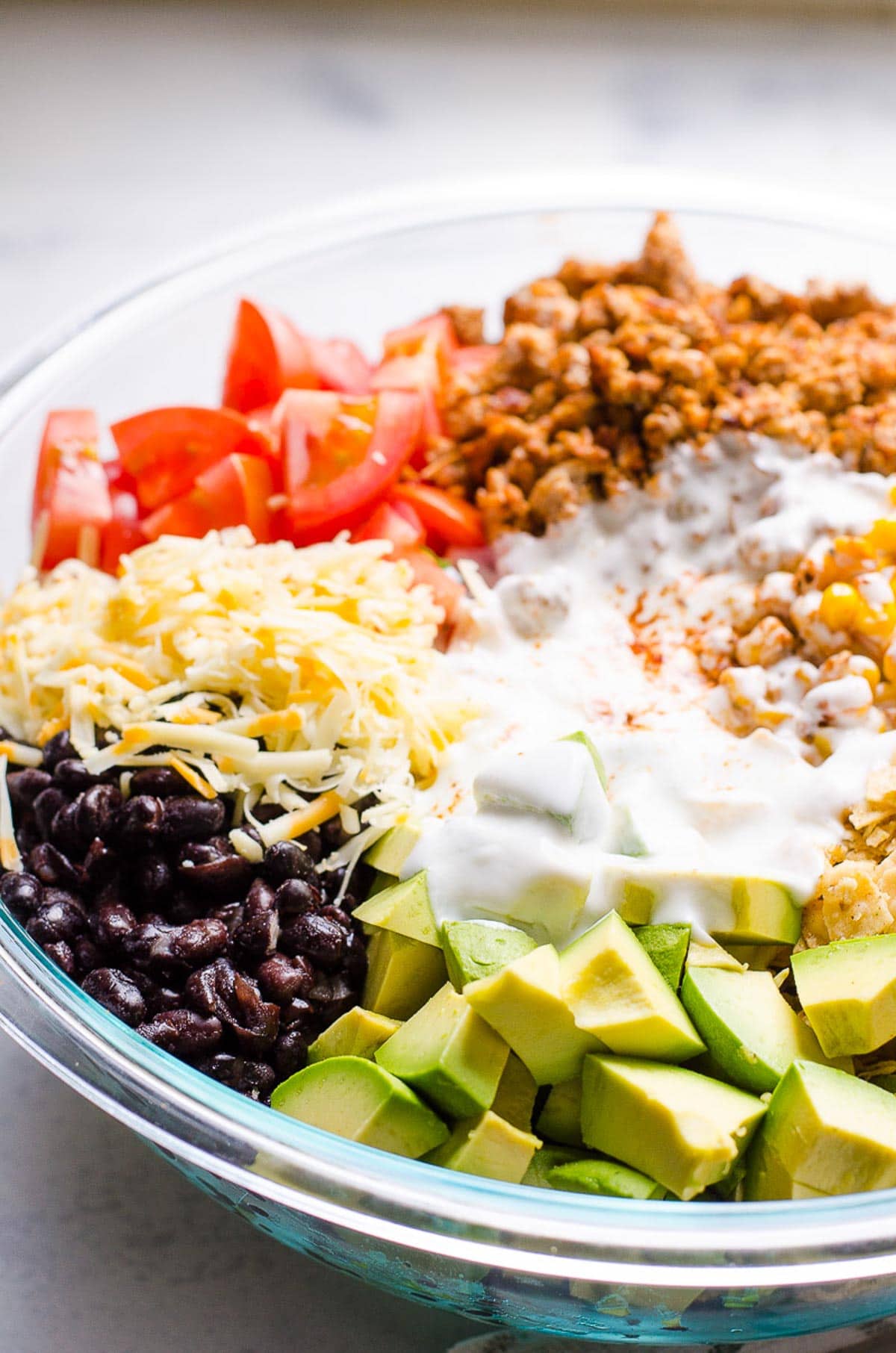 Black beans, avocado, ground turkey, corn, crushed chips, tomatoes, shredded cheese and yogurt in large bowl.