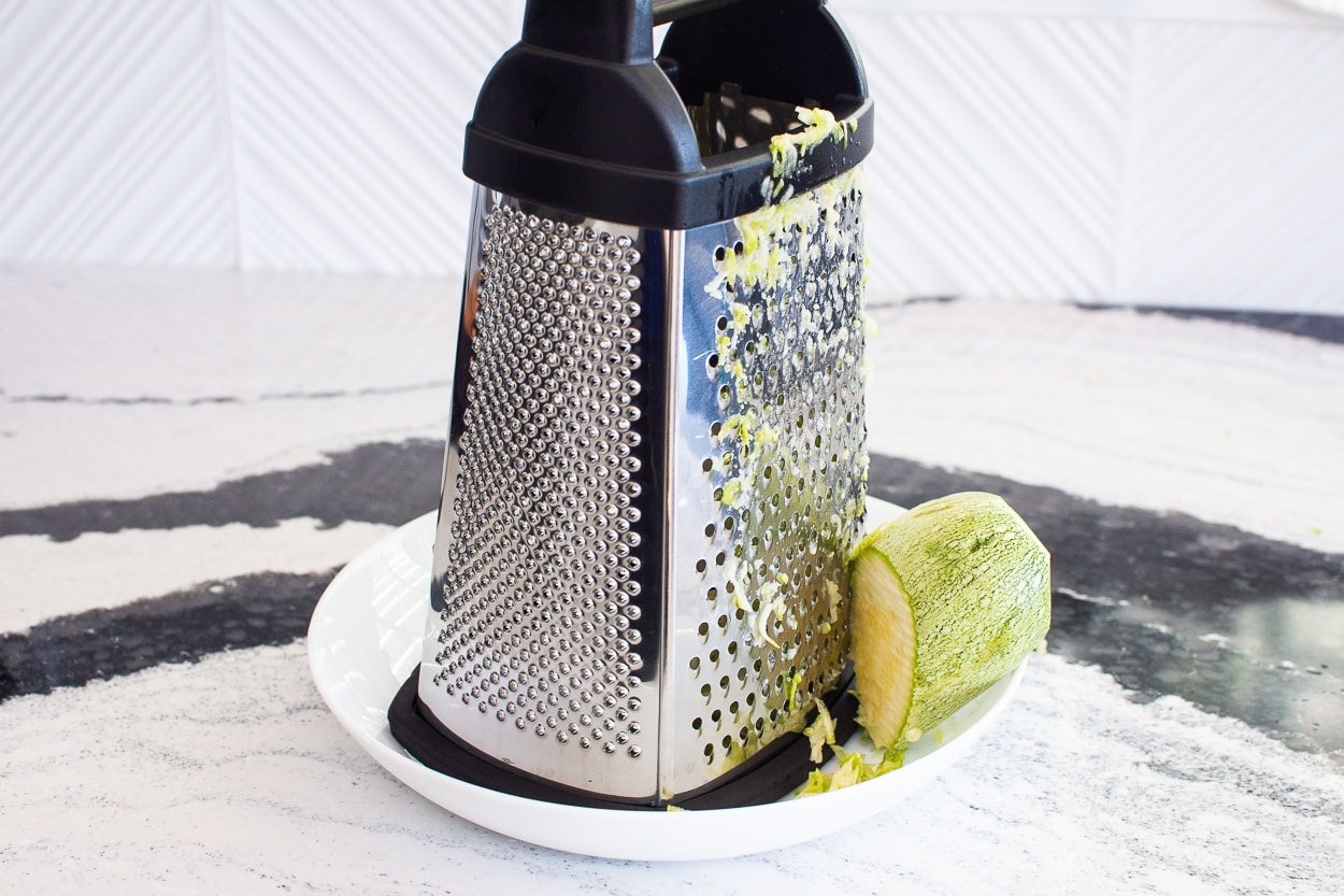 Grater and zucchini on white plate.