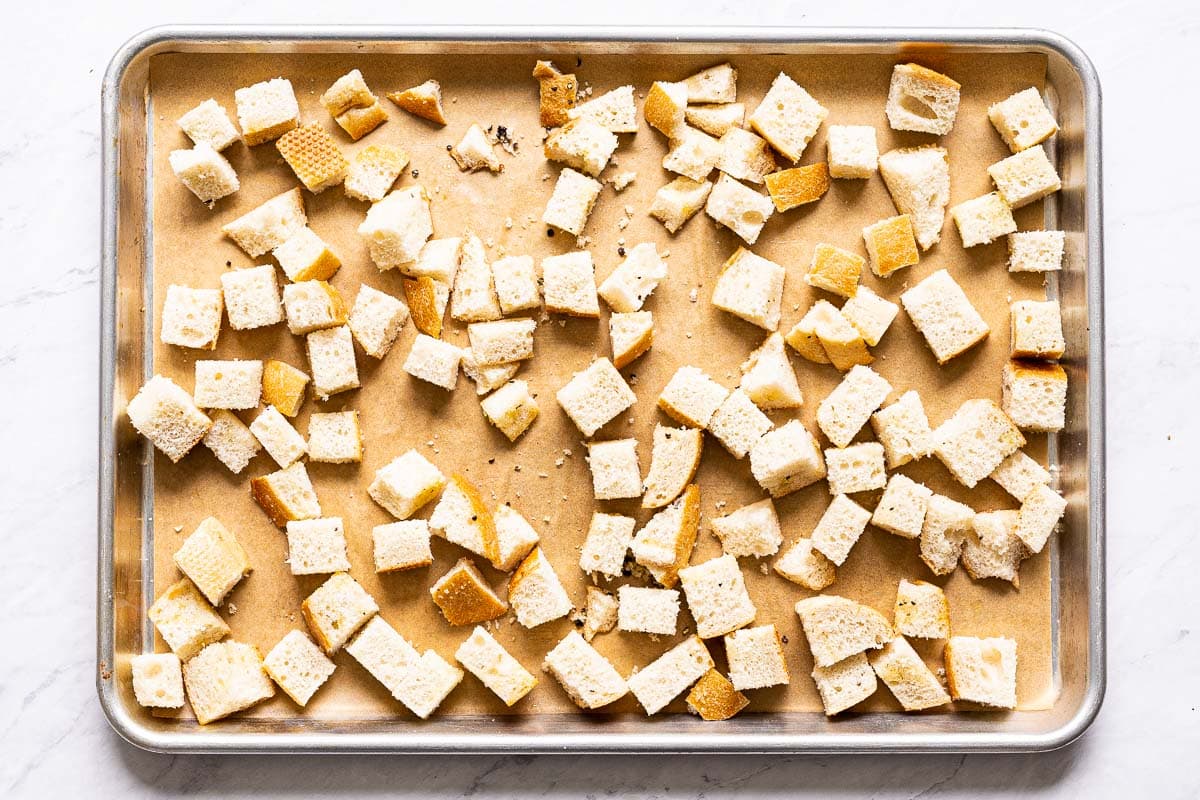 Unbaked sourdough croutons on parchment lined baking sheet.