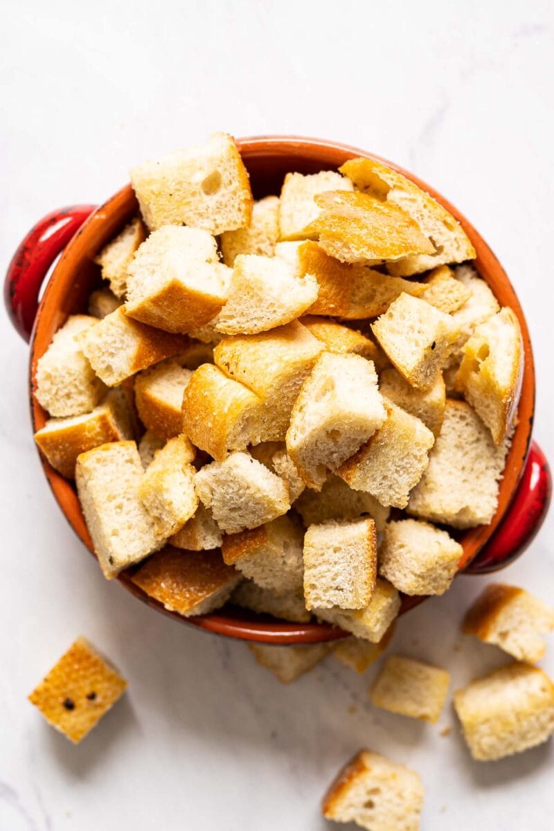 Healthy sourdough croutons in a red bowl with some on counter.