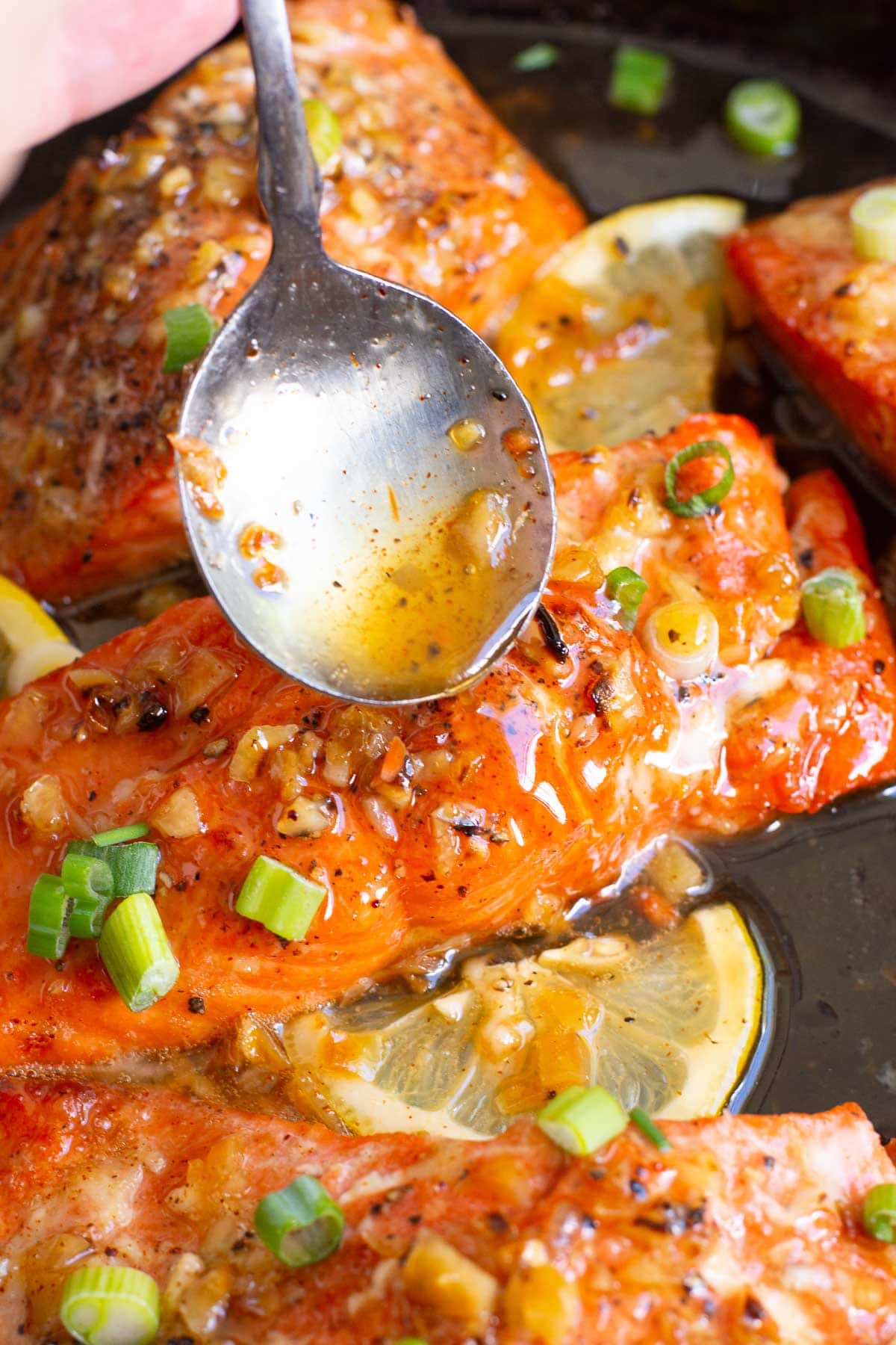 Pouring honey glaze with a spoon over a piece of salmon garnished with green onions.