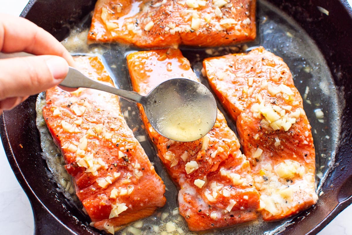 Pouring sauce with a spoon over salmon slices in the skillet.