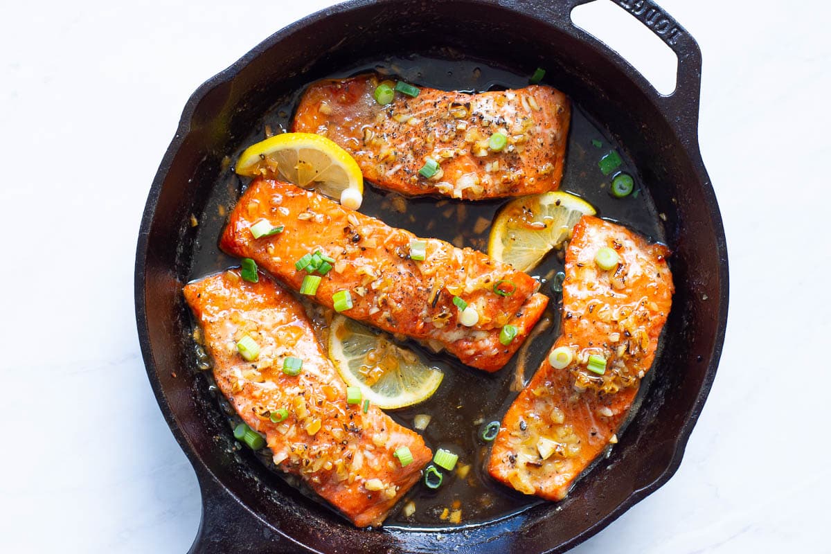 Honey garlic salmon garnished with lemon and green onion in cast iron skillet.
