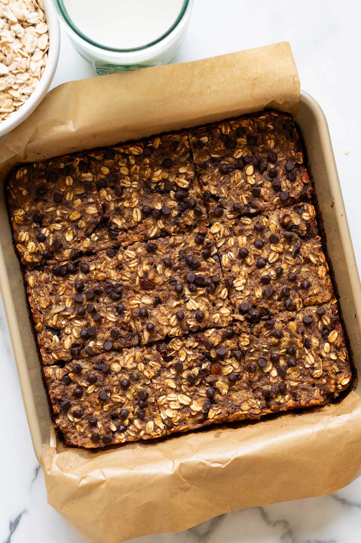 Healthy oatmeal bars in a baking dish. Oats in a bowl and milk in a glass on a counter.