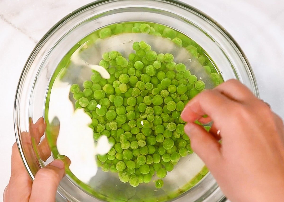 A bowl with frozen peas and hot water.