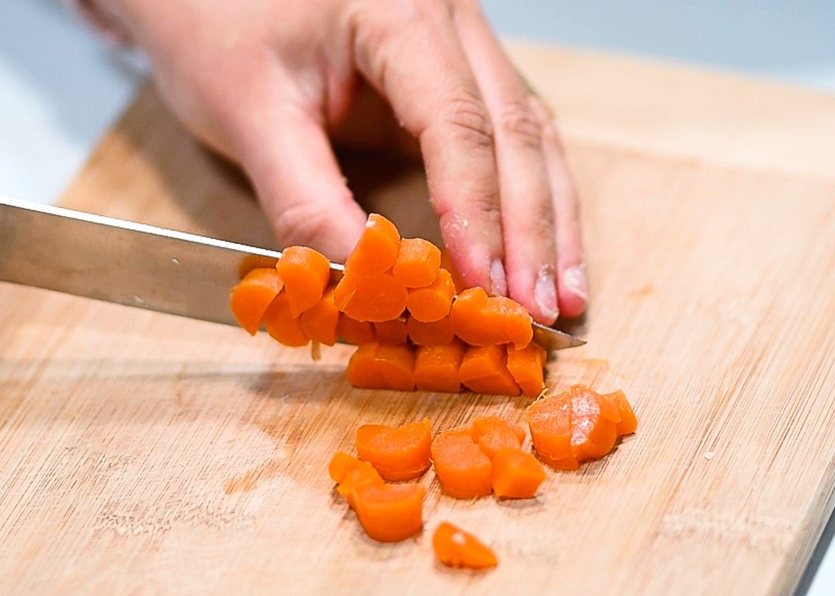 Chopping cooked carrots on a cutting board.