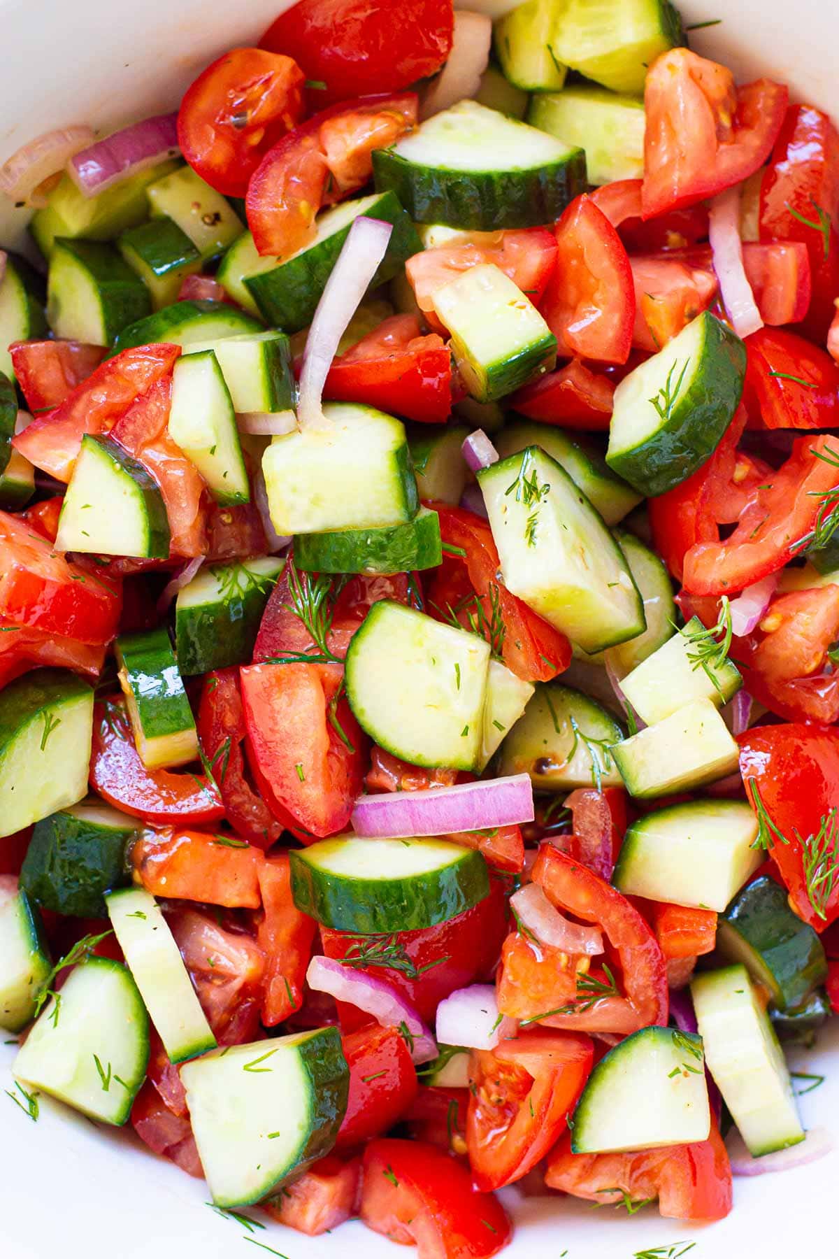 Cucumber and tomato salad with red onion and dill in white bowl.