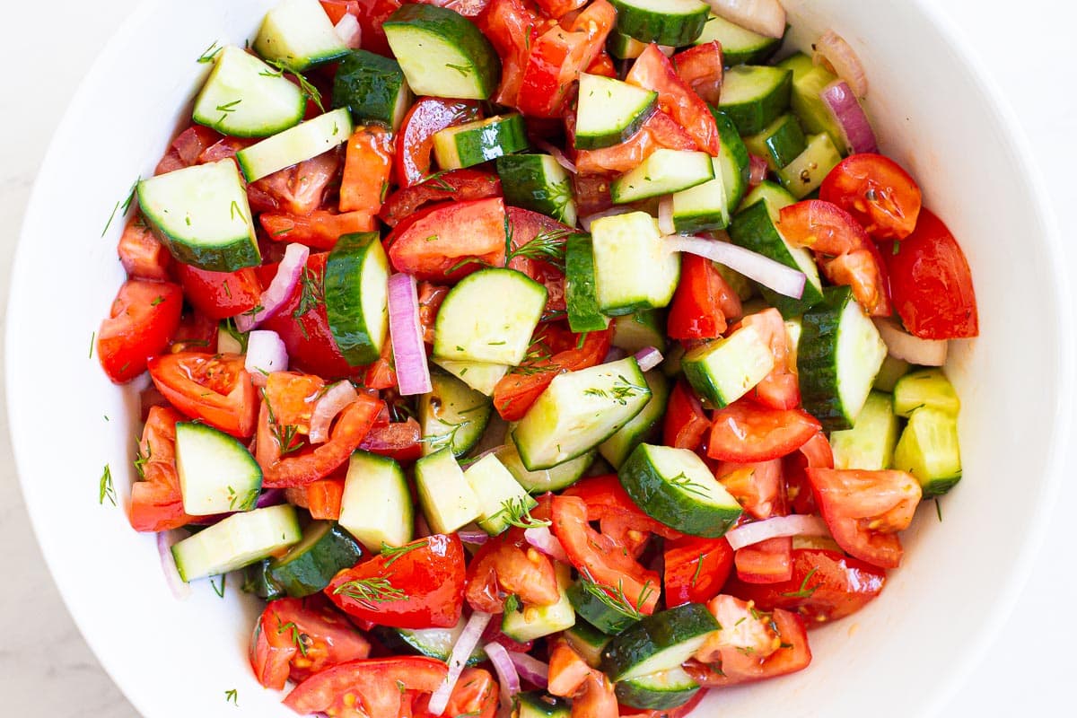 Cucumber and tomato salad with red onion and dill in white bowl.