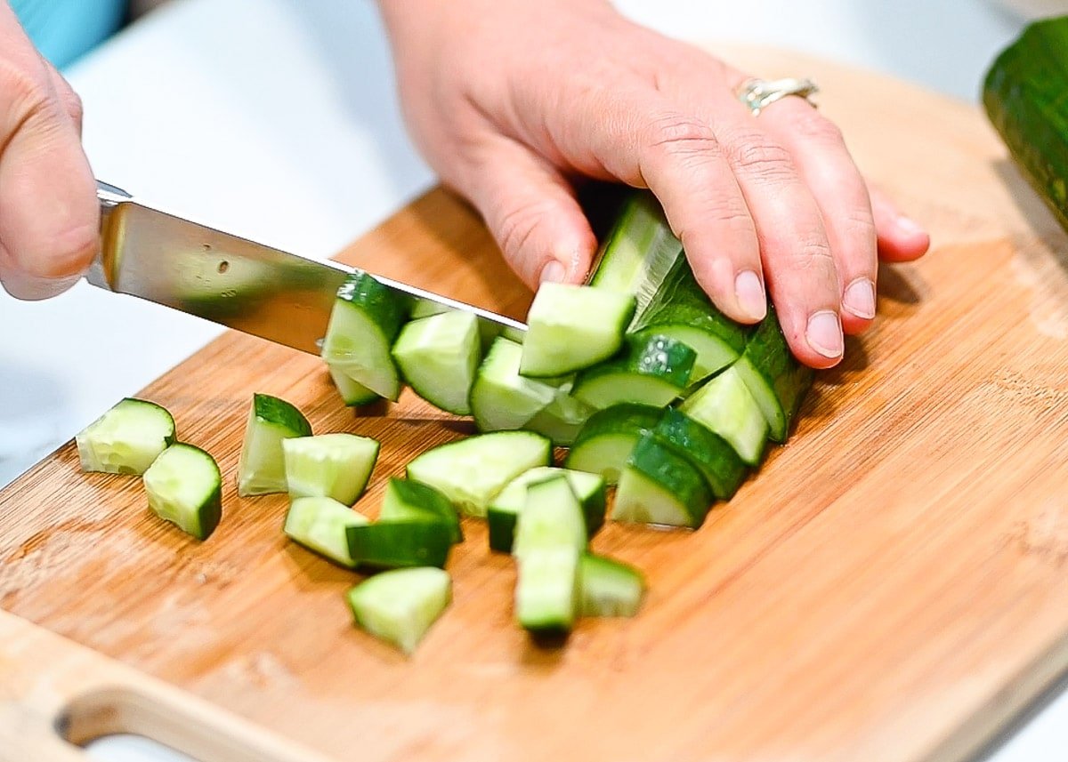 Chopping cucumbers on a cutting board with a knife.
