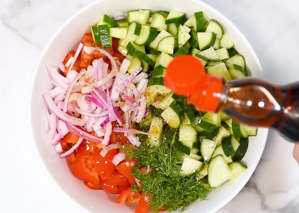 Drizzling sesame oil over a bowl with tomato, cucumber, red onion, dill and spices.