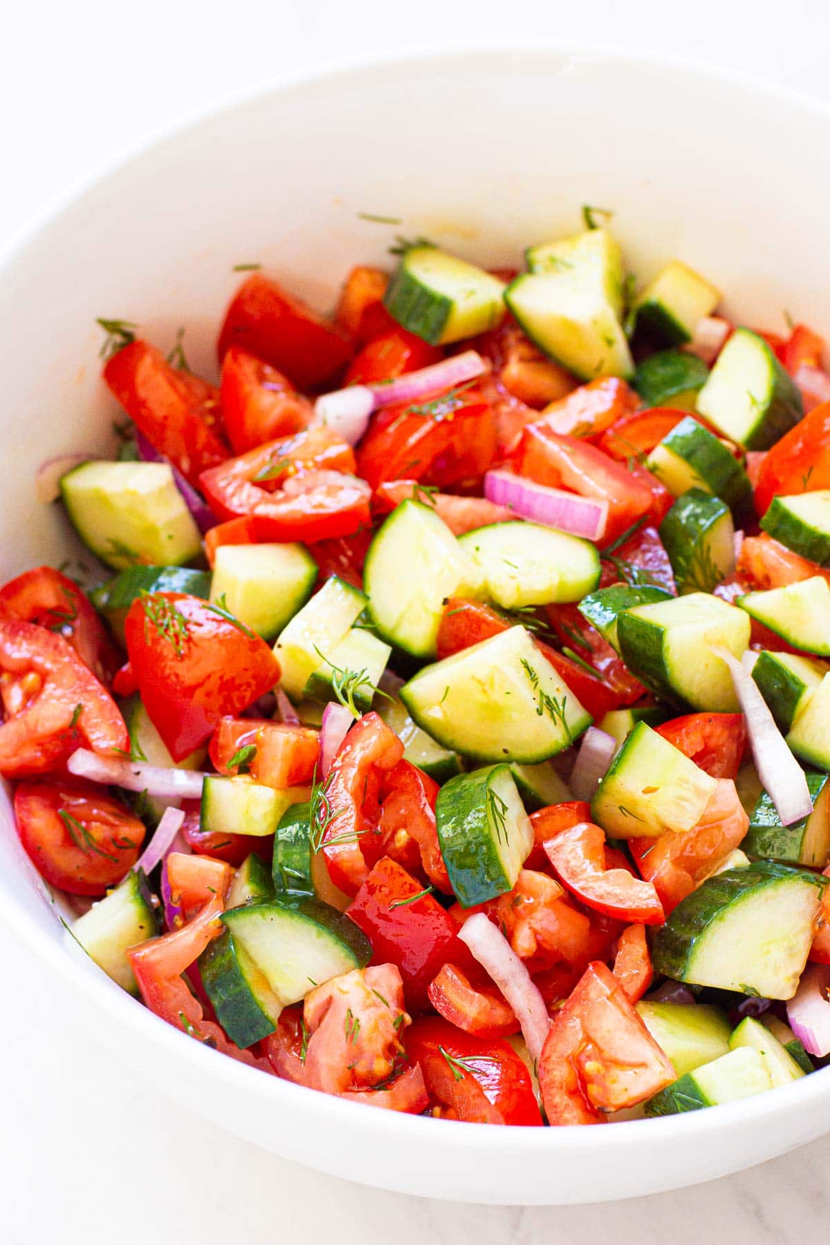 Cucumber and tomato salad with red onion and dill in white bowl.