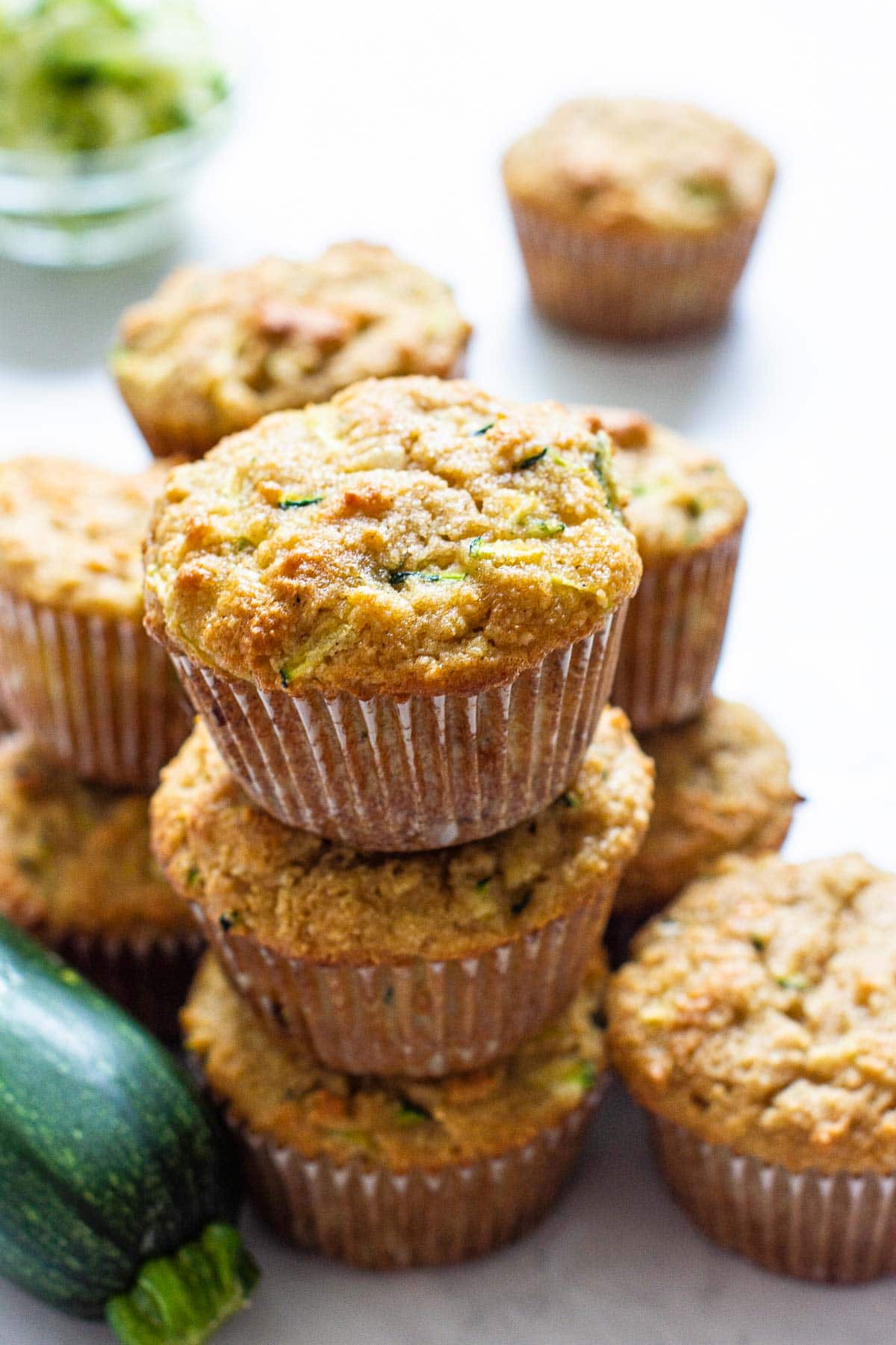 Three stacked almond flour zucchini muffins with a zucchini on a counter.