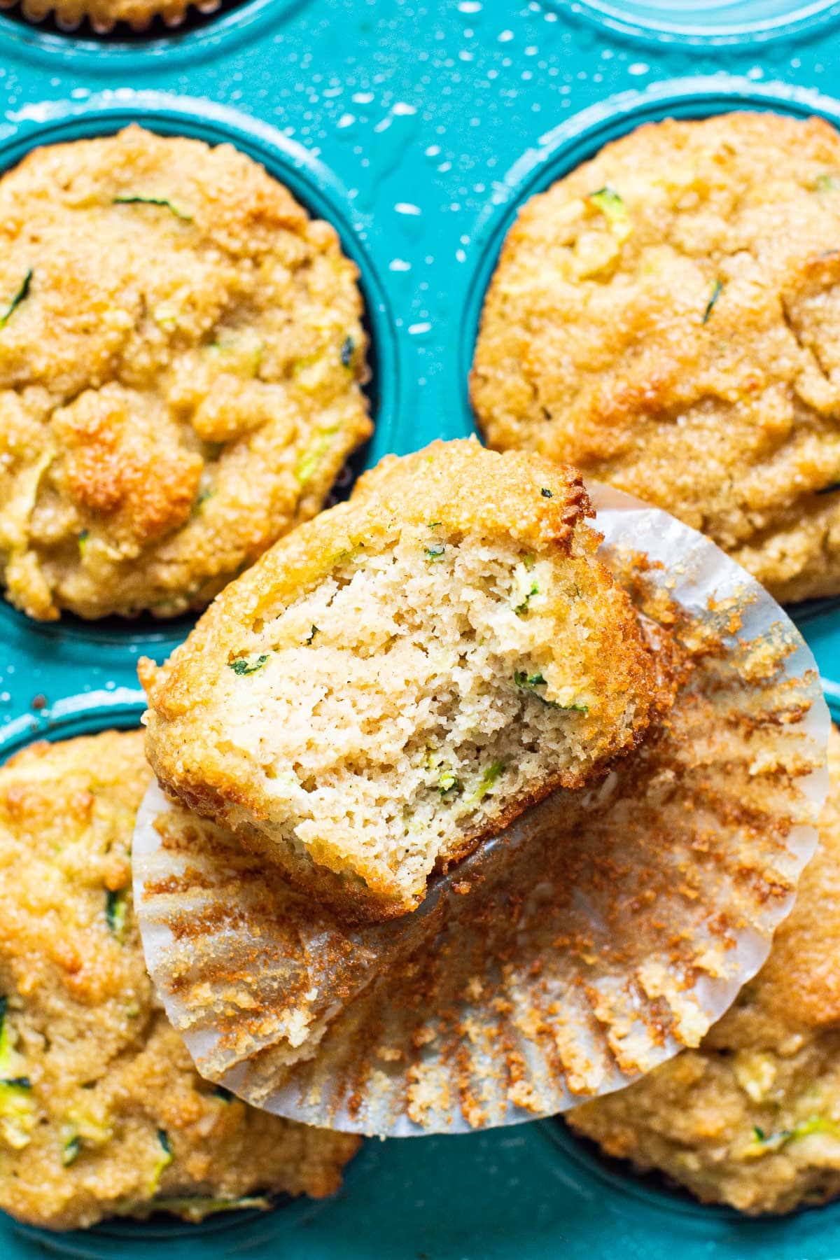 Close up of almond flour zucchini muffins with one unwrapped and a bite missing.