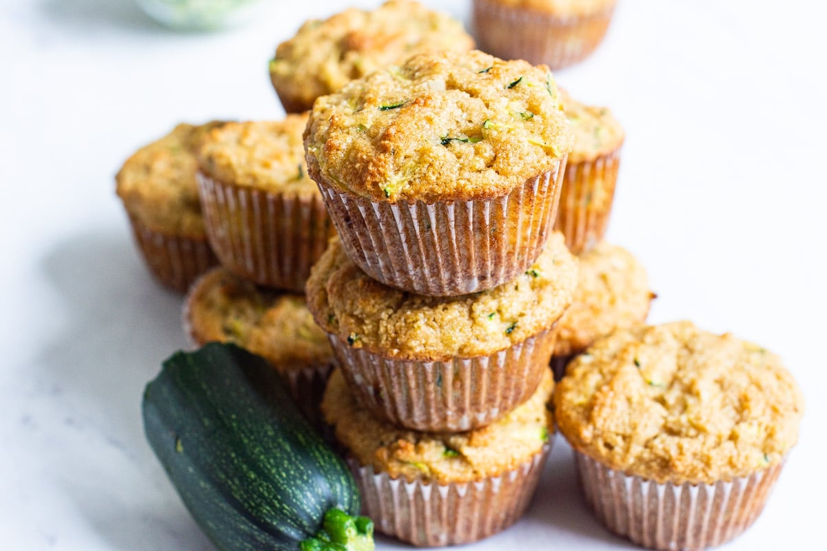 Almond flour zucchini muffins with three stacked. Zucchini near them.