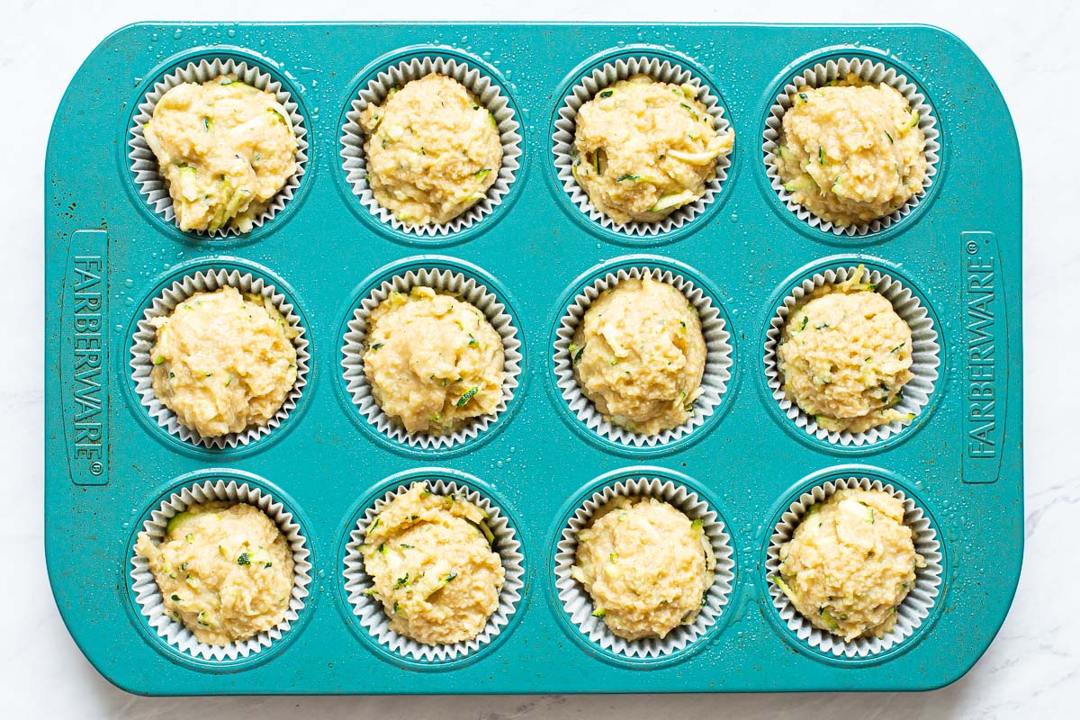 Unbaked muffin batter divided between openings in blue muffin tin.