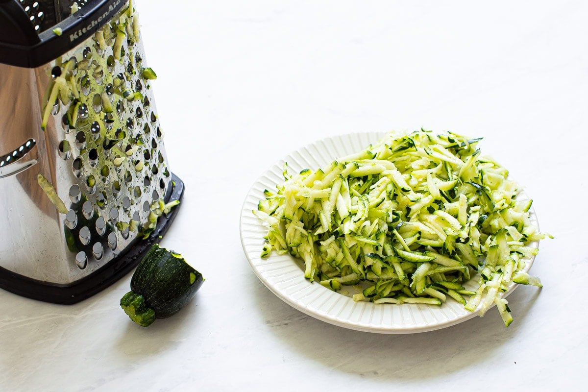Shredded zucchini and box grater on plate. 