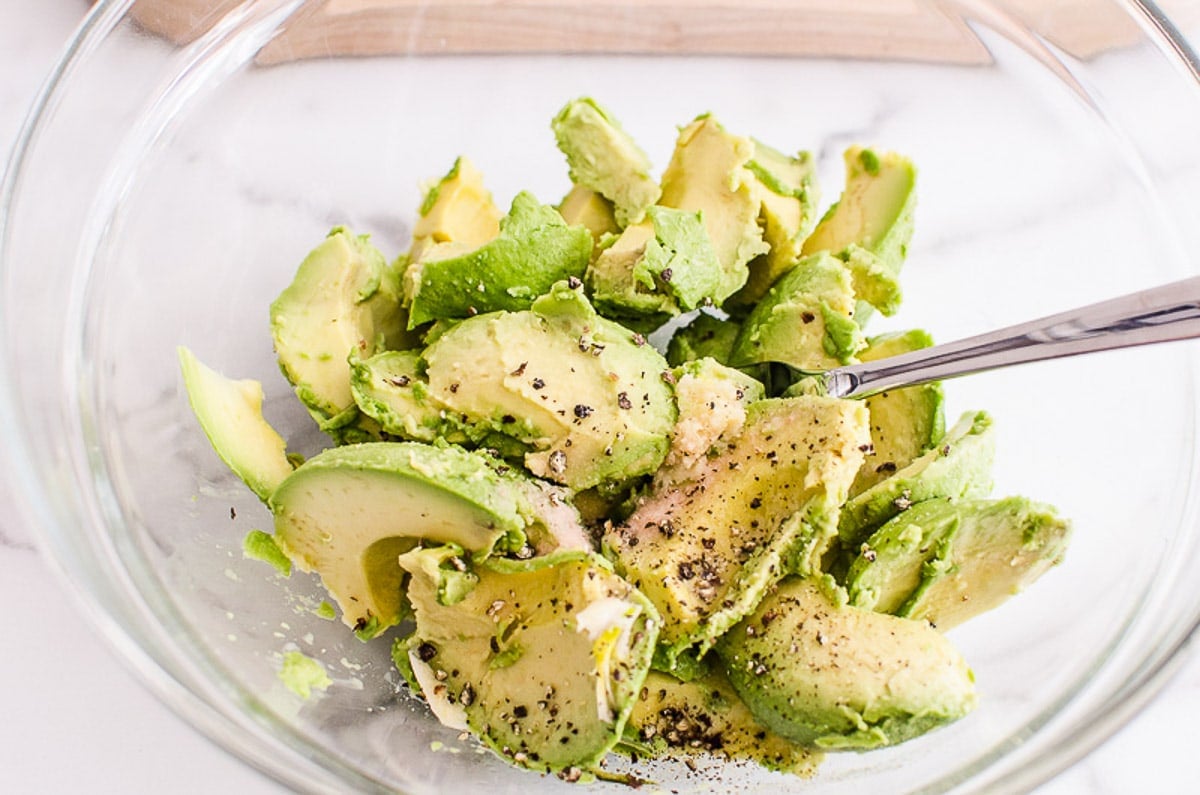 Sliced avocado in a bowl with lemon juice, salt and pepper in a bowl with a fork.