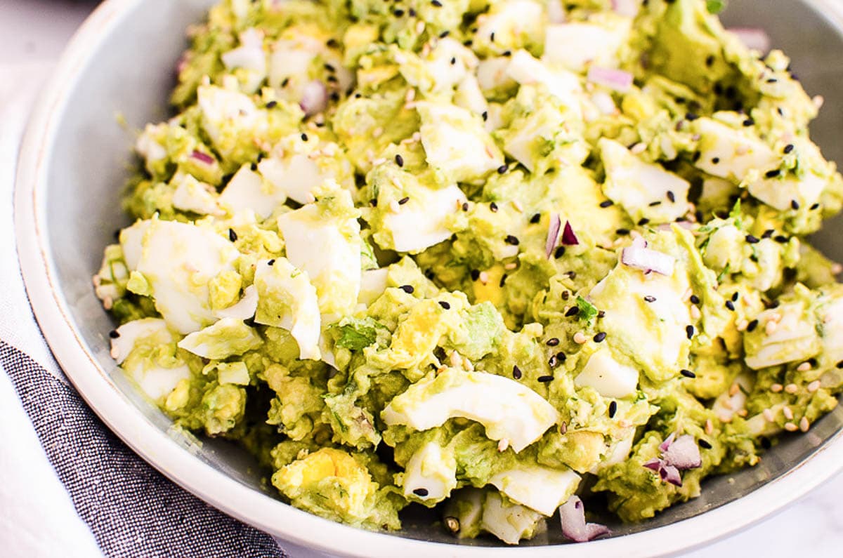 Avocado egg salad garnished with sesame seeds in a bowl.