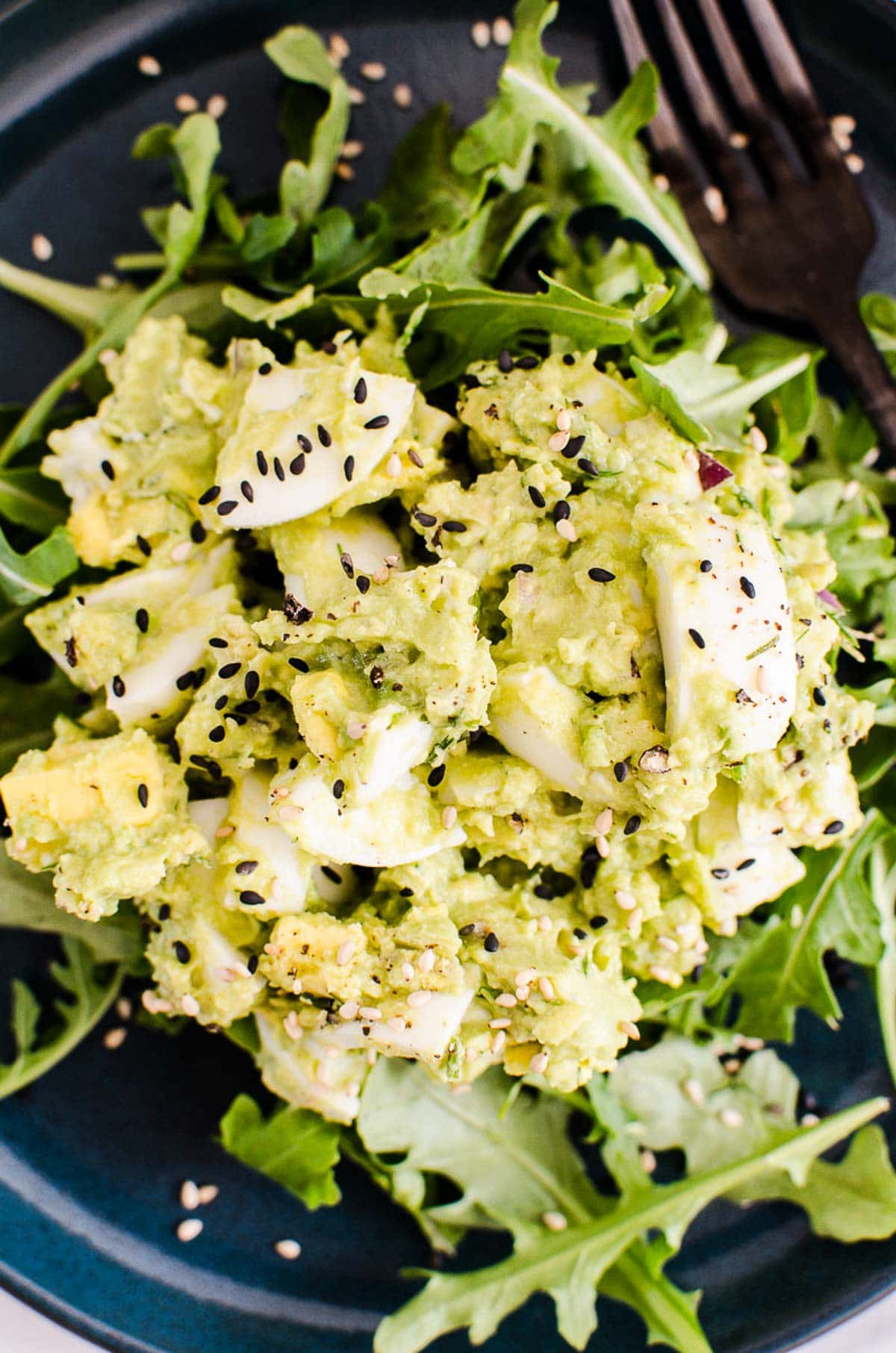 Avocado egg salad served on a bed or arugula and garnished with black sesame seeds.