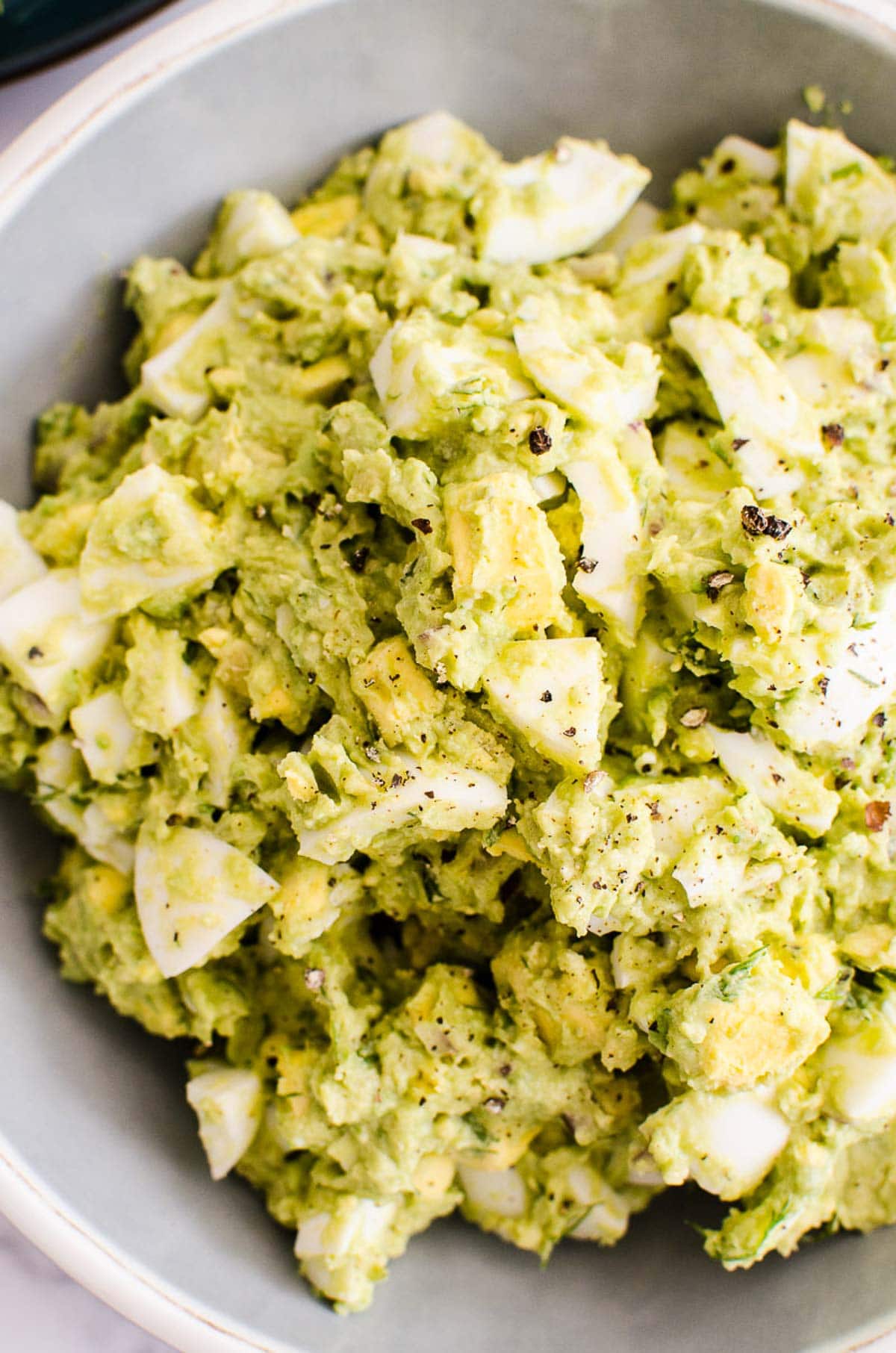 Avocado egg salad in a bowl with black pepper garnish.