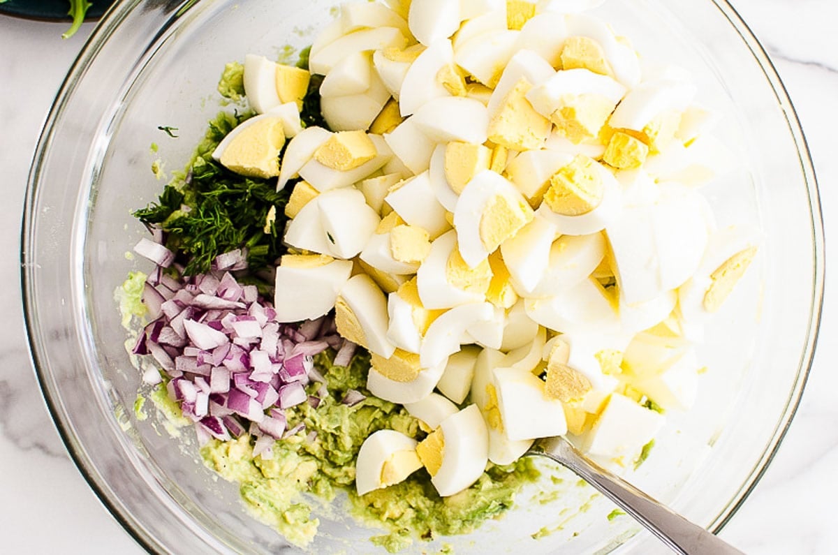 Chopped hard boiled eggs, dill, red onion and mashed avocado in a bowl.