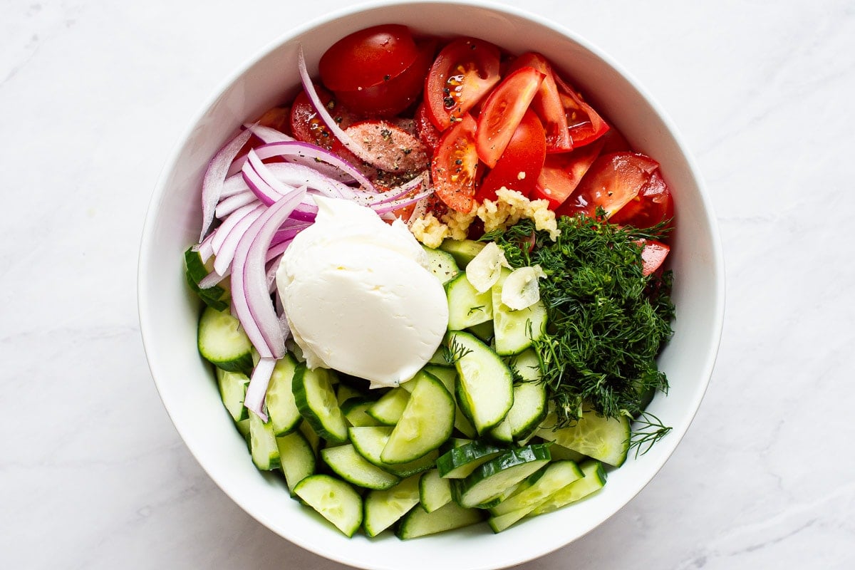 Cucumbers, tomatoes, dill, red onion, and sour cream in bowl.
