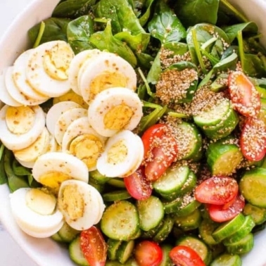 Spinach in a bowl with eggs, cucumber, tomato and sesame seeds.