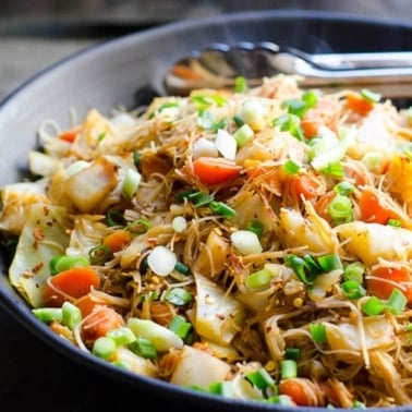 Cabbage stir fry with noodles, carrots and green onions in black bowl.