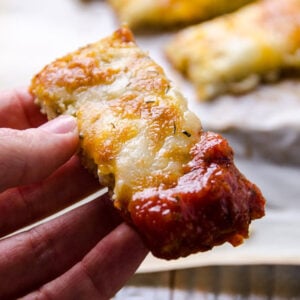 A hand holding cauliflower breadsticks dipped in salsa.