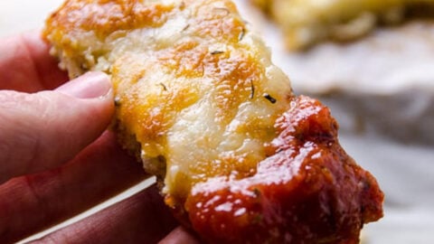 A hand holding cauliflower breadsticks dipped in salsa.
